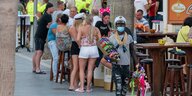 Mallorca: Sonnebrillenverkäufer mit Mundschutz, im Hintergrund eine Gruppe trinkender Touris