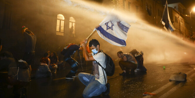 ein Demonstrant mit israelischer Flagge im Strahl eines Wasserwerfers