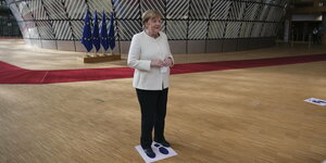 Merkel steht auf einer Bodemarkierung, im Hintergrund EU-Fahnen