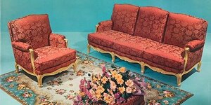Rote Couchgarnitur auf türiksfarbenem Teppich. Das Foto davon ist goldgerahmt.
