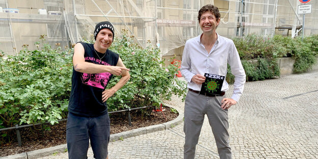 Joshi von der Berliner Punkrock Band ZSK und Christian Drosten freuen sich bei der Übergabe einer Schallplatte. Sie stehen mit ein bisschen Abstand auf einem Berliner Bürgersteig.