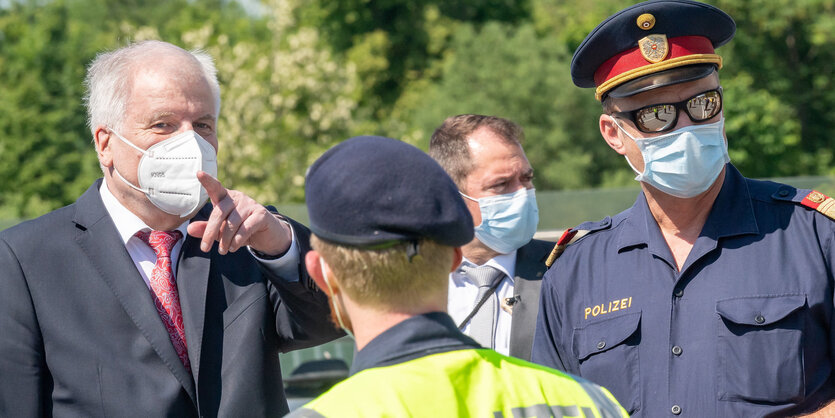 Horst Seehofer (CSU, l), Bundesinnenminister, trägt Mundschutz, während er sich am bayerischen Grenzübergang Freilassing zwischen Deutschland und Österreich mit einem österreichischen Grenzpolizisten unterhält