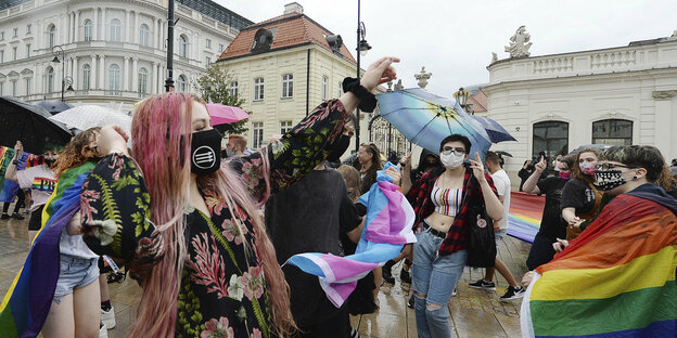 Junge Menschen tanzen auf der Straße im Regen in regenbogenfarbene Fahnen gehüllt