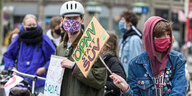 Zwei Frauen mit Atemmaske halten ein Schild hoch. darauf steht: ÖPNV statt SUV