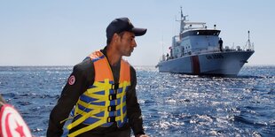 Ein Uniformierter mit Warnweste auf einem Boot auf hoher See.