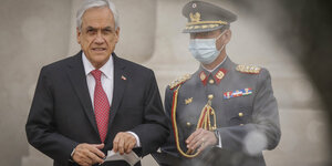 Ein Soldat mit Mundschutz steht neben einem Mann in Anzug, der einen Mundschutz in der Hand hält.