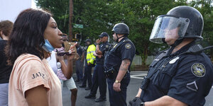 Eine schwarze Frau mit T-Shirt und ein weißer Mann in Polizeiuniform stehen sich gegenüber.