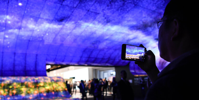 EIn Mensch hält sein Smartphone in der Hand und fotografiert einen blauen Hintergrund.