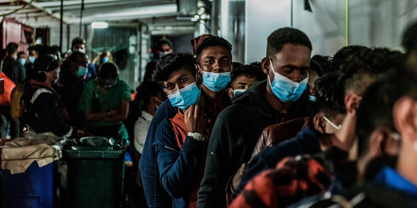 Auf dem Deck eines Schiffes sitzten dircht gedrängt Menschen mit Mund-Nasen-Masken