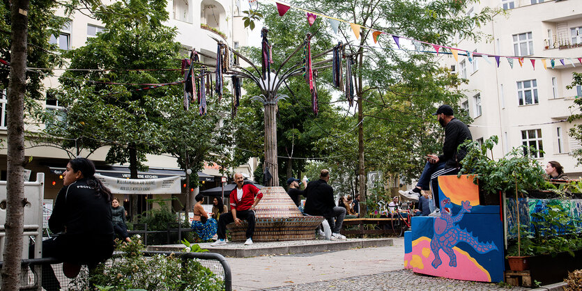 Einige Menschen sitzen entspannt auf einem Platz in Neukölln