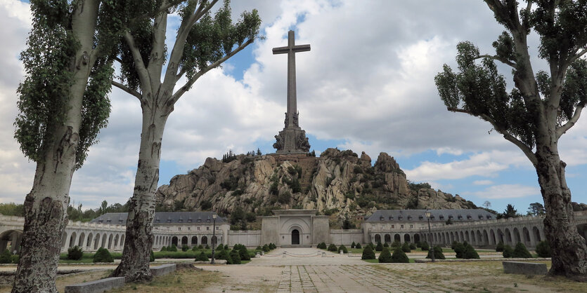 Ein Berg, auf dem ein mächtiges Betonkreuz steht. Davor ein symetrisch, zweiflügelig angelegter Bau. Im Zentrum das Tor des Mausoleumsserg hinein.