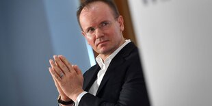 Markus Braun sitzt neben einem Wirecard-SChild und faltet die Hände