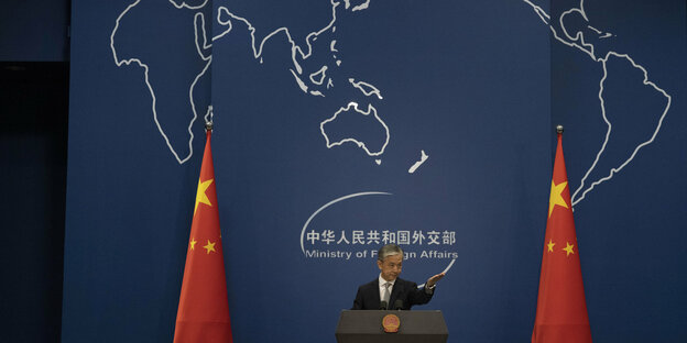 Ein Mann an einem Rednerpult, rechts und links von ihm chinesische Fahnen, hinter ihm ist eine Weltkarte
