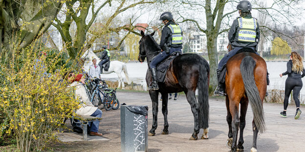 Zwei Polizisten auf Pferden sprechen mit Menschen auf Parkbänken.