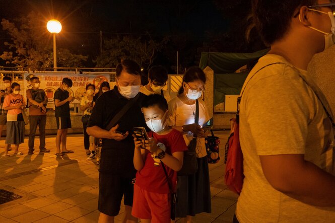 Hongkonger*innen mit Mund-Nasen-Maske stehen draußen Schlange