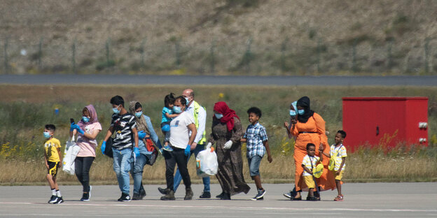 Eine Menschengruppe mit Mundschutzmasken laufen am laufen am Flughafen
