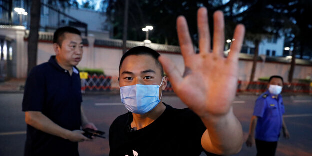Ein Mann mit Gesichtsmaske versucht, mit der Hand die Kamera des Fotografen zu verdecken.