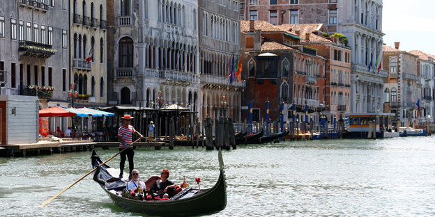 Eine Gondel mit zwei Menschen und dem Gondelführer scheimmt vir Venedig