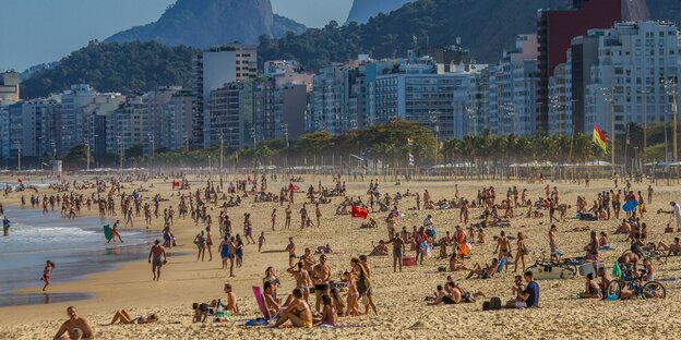 Ein voller Strand in Rio de Janeiro, im Hintergrund Wohnblocks und Berge