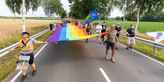 Demonstrant*innen ziehen mit einer riesigen Regenbogenflagge über eine Landstraße