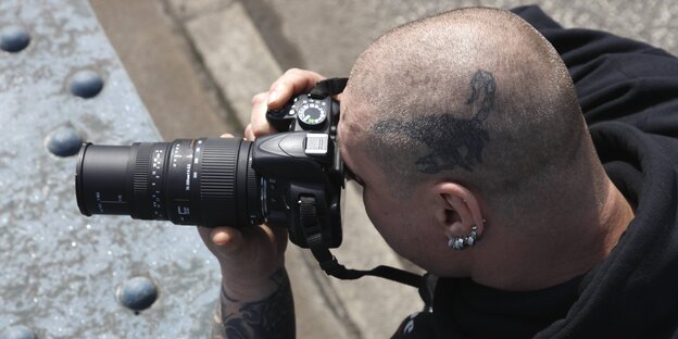 Ein tätowierter Glatzkopf fotografiert mit einem Teleobjektiv