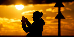 Eine Frau fotografiert die untergehende Sonne am Strand der Insel mit ihrem Smartphone