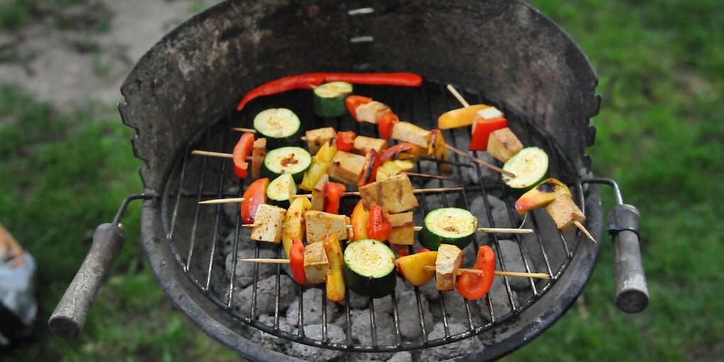 Auf einem Holzkohlegrill liegen gemüsespiesse