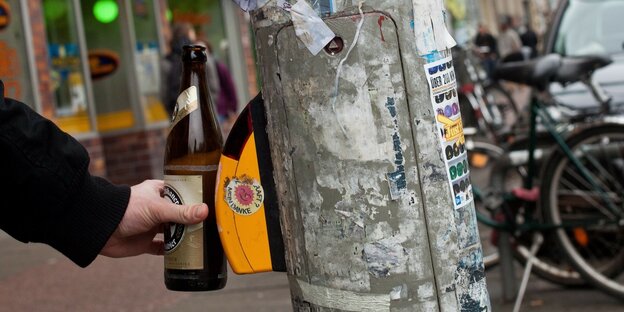 Eine Flasche Bier in der Hand eines Fußgängers berührt den Schalter einer Ampel
