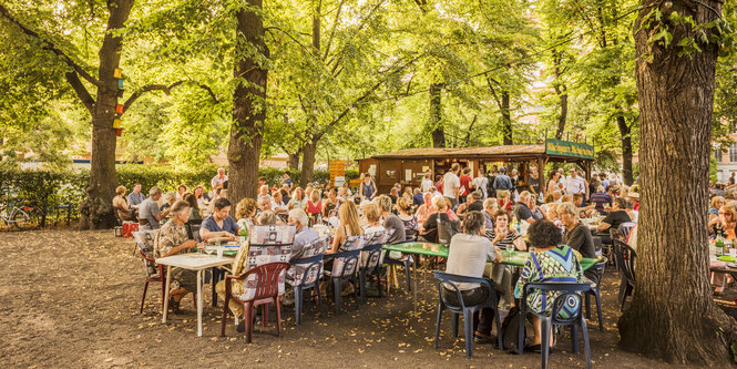 Als es noch kein Corona gab: Rheingauer Weinbrunnen am Rüdesheimer Platz. Menschen, die unter Linden an Tischen sitzen und Wein trinkenkenmsich unter ucg die schnesh