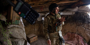 Ein Soldat steht in einer Art Steinhöhle, wie in einem Front-Graben und bewegt die Hand, als würde er etwas abwägen