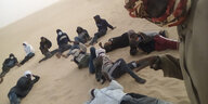 Mehrere Menschen sitzen oder liegen im Sand in der Wüste.