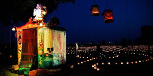 Ein beleuchtetes Zelt mit einem Menschen obenauf und viele Kerzenlichter drumherum: eine Stene aus dem Stück "Die große Reise" des Theaters Anu auf dem Tempelhofer Feld