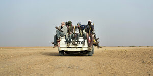 Junge Männer sitzen auf einem Lastwagen der in die Wüste fährt