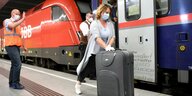 Ein Zug der ÖBB an einem NBanhsteig, davor eine Frau mit Koffer und Maske
