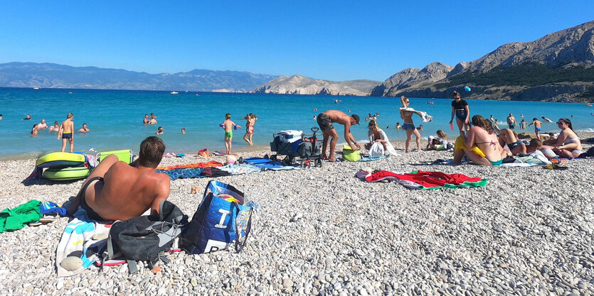 Urlauber liegen an einem Kiesstrand in der Sonne