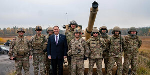 Mike Pompeo steht mit Soldaten in Uniform vor einem Panzer