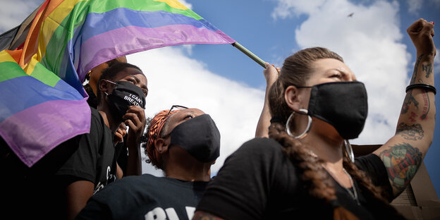Demonstrierende Personen mit Mundschutz und Regenbogenfahne