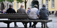 Alte Männer und Frauen sitzen, von hinten zu sehen, auf einer Parkbank.