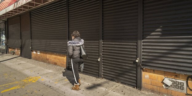 Eine Frau geht an einer Fensterfront entlang, die Fenster sind mit Rolläden verschlossen