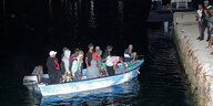 Mehrere Flüchtlinge sitzen in einem Boot und legen am italienischen Hafen in Lampedusa an