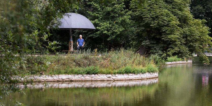 In grüner Berliner Parklandschaft ein Wetterpilz und darunter stehend Klaus Herda