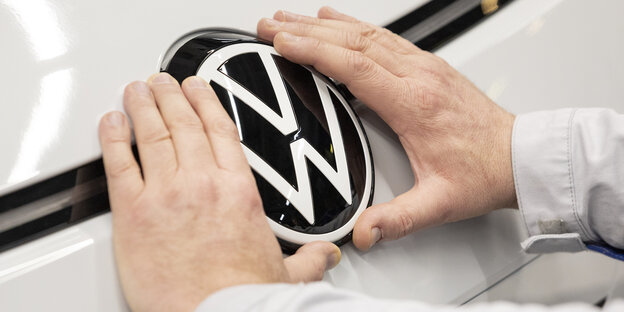 Zwei Hände befestigen das VW-Logo auf der Kühlerhaube eines Autos