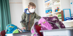 Ein Schüler mit Maske stellt seinen Schulranzen auf den Tisch