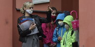 Eine Lehrerin mit Masken und mehrere Schülerinnen mit Masken stehen im Klassenzimmer