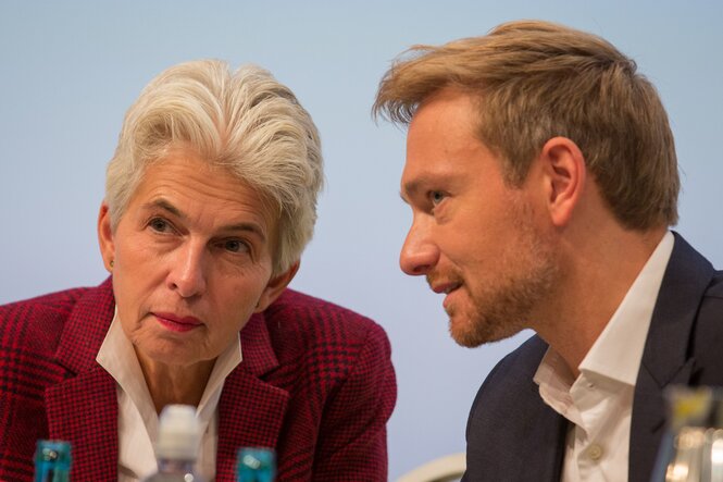 Die Oberkörper von Christian Lindner und Marie Strackzimmermann sind zueinander geneigt. Lindner hat die Lippen geöffnet, als spräche er, Strack-Zimmermann hört zu