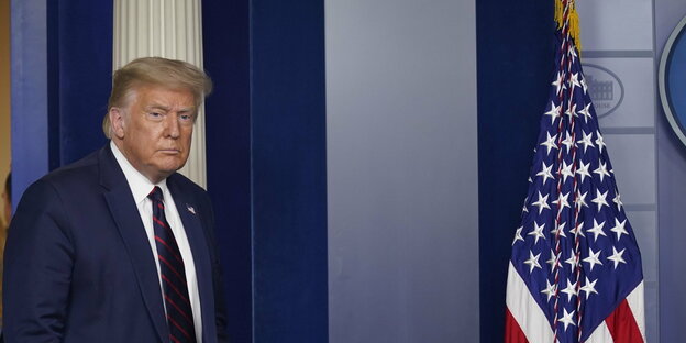 Donald Trump läuft in einen Raum mit einer US-Fahne