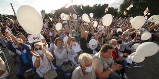 Eine Menge von Menschen mit Mundschutz und weißen Luftballonen.