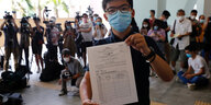 Der prodemokratische Student Joshua Wong steht mit Maske vor der Presse und zeigt seine Registrierung für die kommende Wahl
