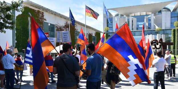 Die armenische Demonstration vor dem Kanzlerinnenamt. Menschen mit Flaggen stehen gemeinsam vor dem Haus. Es sind Flaggen von Berg-Karabach: Eine armenische Flagge mit einem weißen Dreieck.