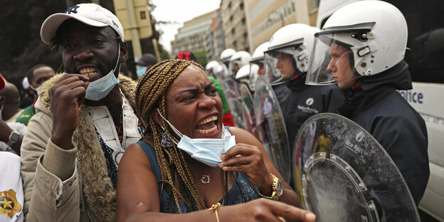Demo-Teilnehmende schreien mit runtergezogenem Mundschutz Polizisten an